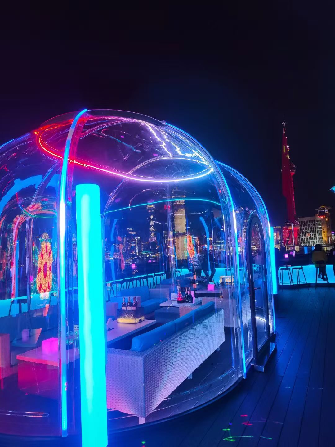 Polycarbonate dining dome on a Shanghai rooftop at night, city skyline behind