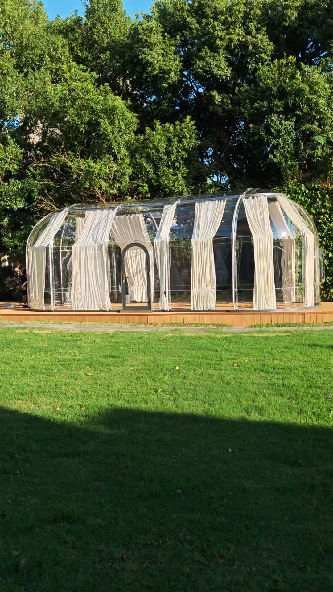 Extended oval Domevora dome in a garden with white curtains on a timber platform