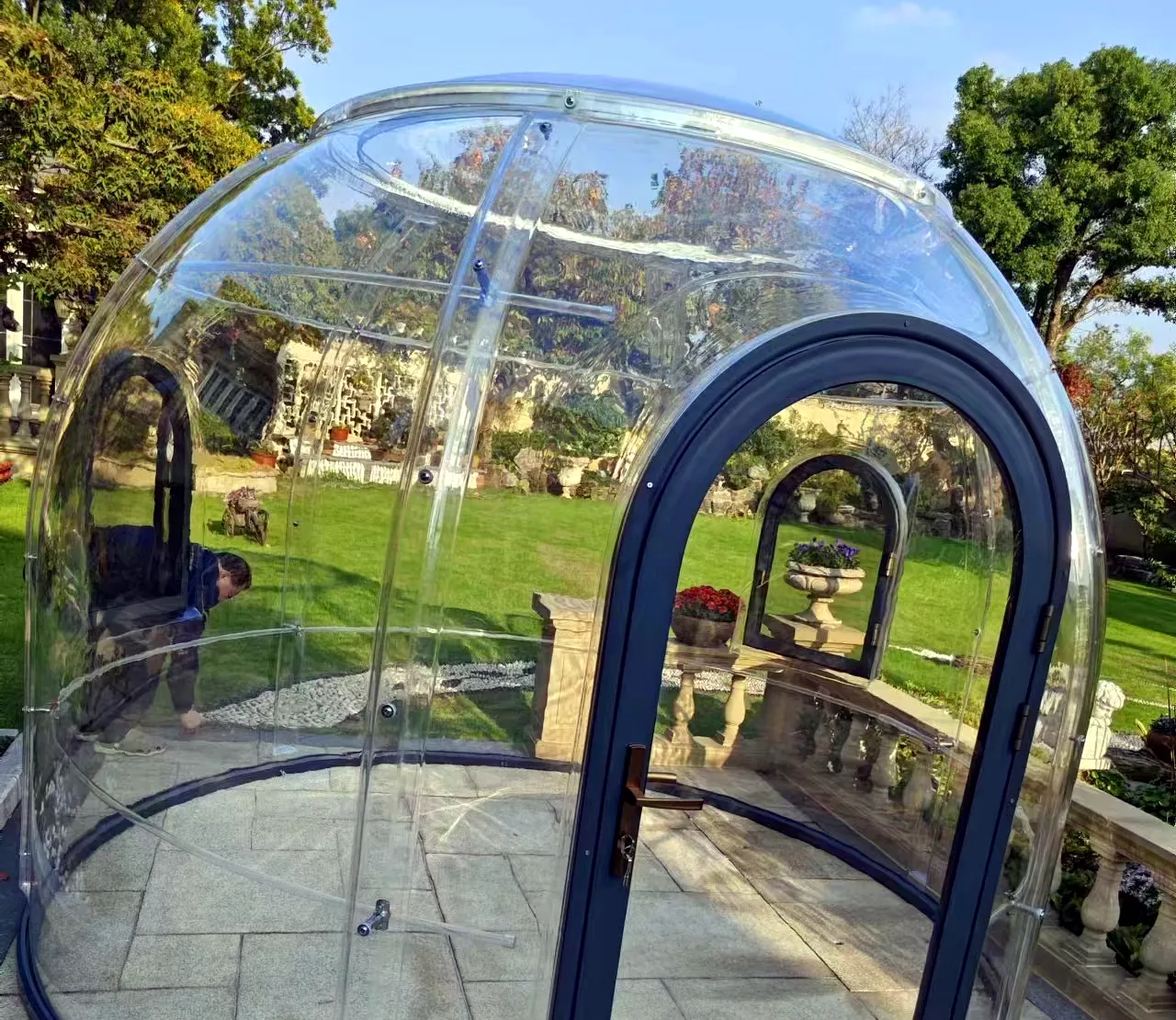 Round 3.0 m clear polycarbonate dome on a stone terrace beside a lawn in a landscaped garden