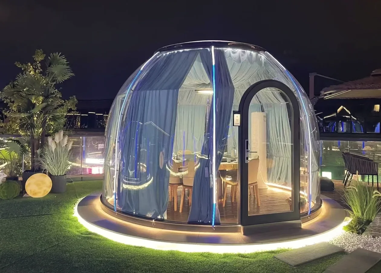 Round 3.5 m High clear polycarbonate dome: a rooftop garden at night, set up for dining with LED base lighting