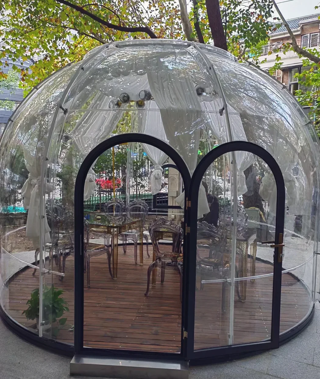 Round 4.0 m High clear polycarbonate dome: a paved garden with a timber floor and dining chairs inside