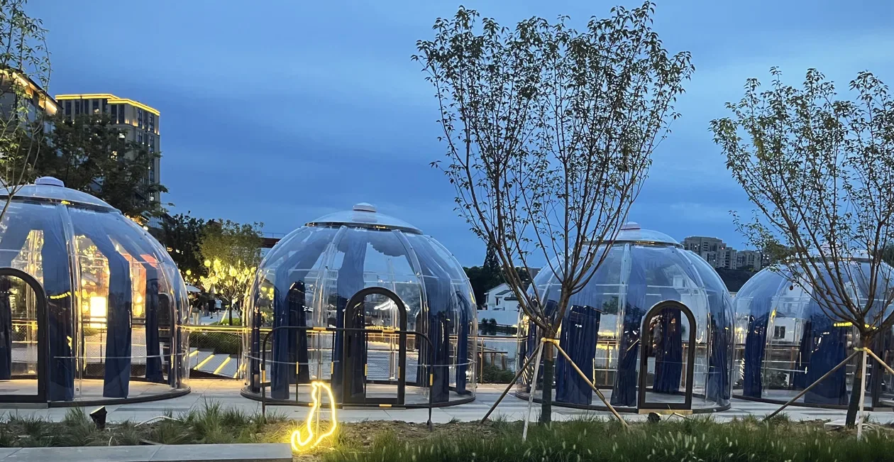 Round 5.0 m Domevora dome, client installation: a row of dining domes on an evening plaza, between young trees