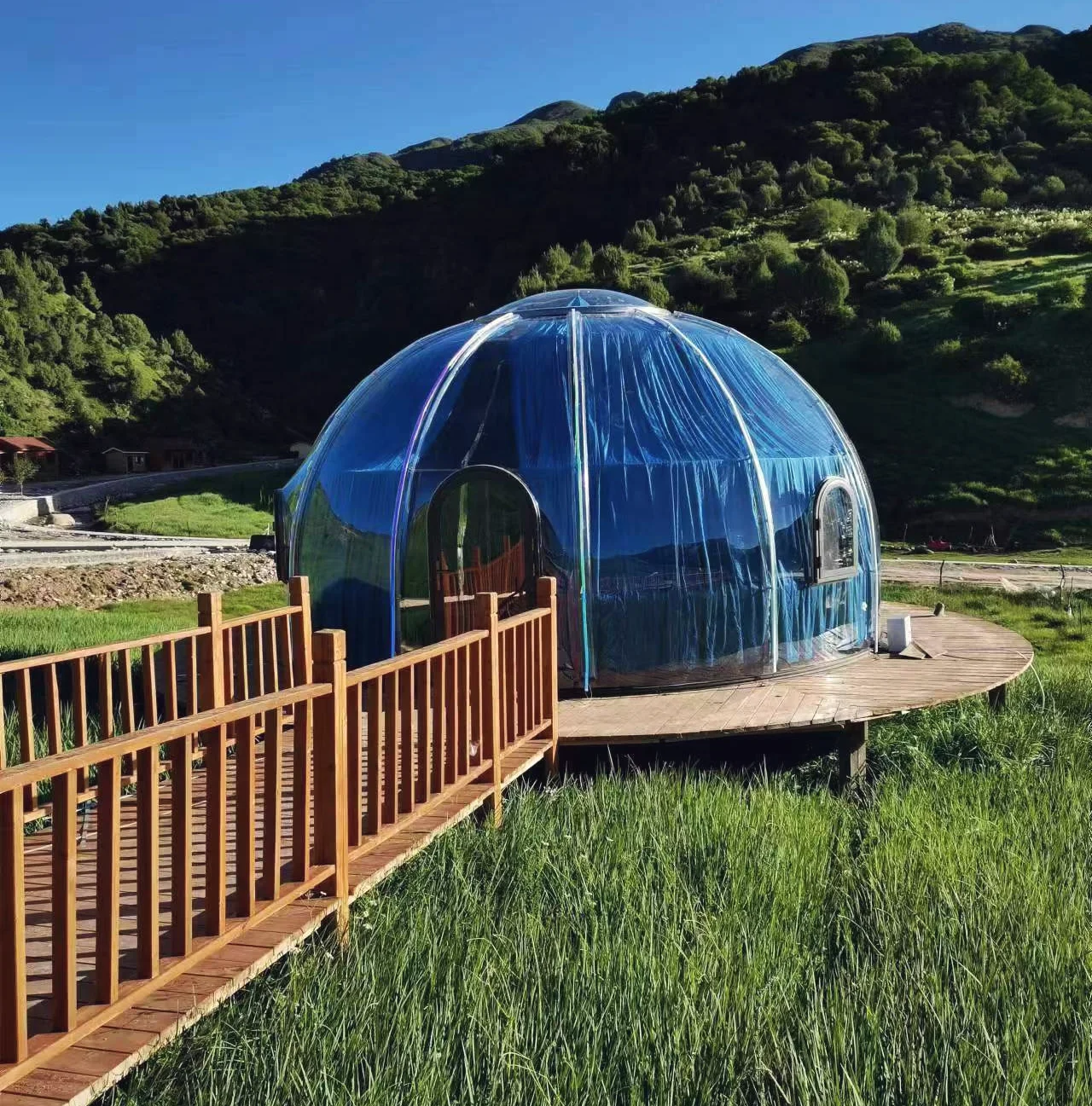 Round 6.0 m clear polycarbonate dome on a hillside deck reached by a timber walkway, client installation